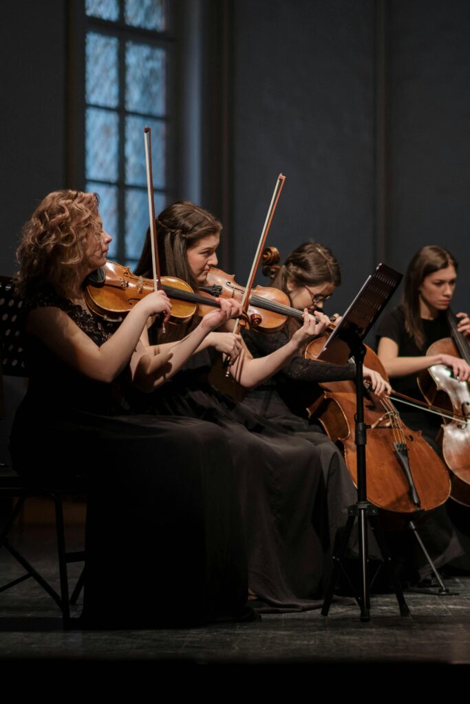 A group of women playing violins and cellos in a classical music performance indoors.